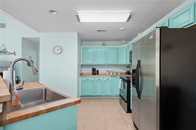 kitchen featuring electric stove, butcher block counters, freestanding refrigerator, light tile patterned flooring, and a sink