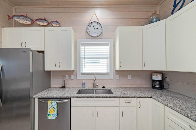 kitchen featuring white cabinetry, sink, stainless steel appliances, and wooden walls