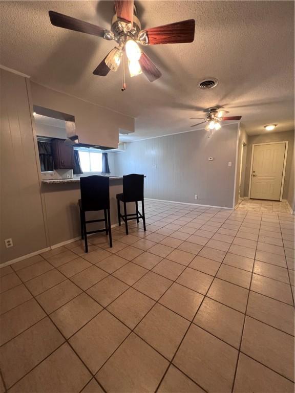 5825 San Saba Dr, Corpus Christi, TX 78407 - kitchen featuring a textured ceiling, light tile patterned flooring, a ceiling fan, and a breakfast bar area