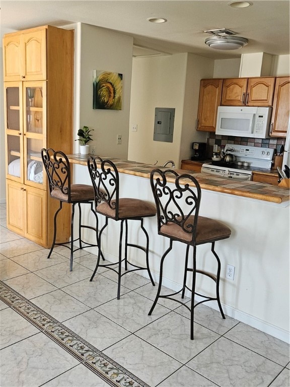 kitchen with electric panel, kitchen peninsula, a breakfast bar area, tasteful backsplash, and white appliances