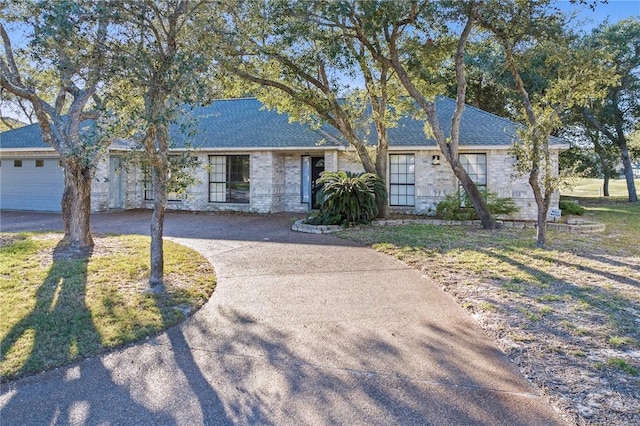 ranch-style house with concrete driveway, a garage, roof with shingles, and a front lawn