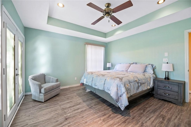 bedroom featuring a raised ceiling, recessed lighting, wood finished floors, and baseboards