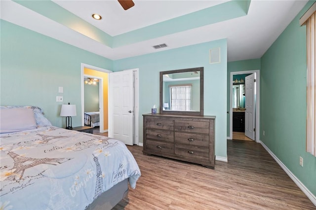 bedroom featuring visible vents, a ceiling fan, a tray ceiling, wood finished floors, and baseboards