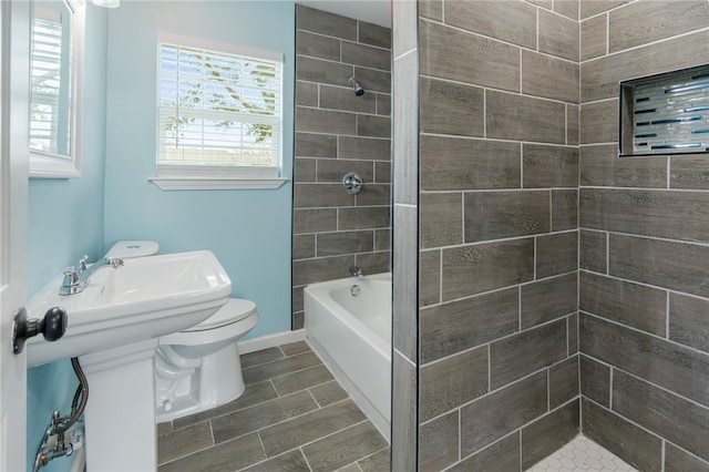 bathroom with tiled shower / bath, toilet, and baseboards