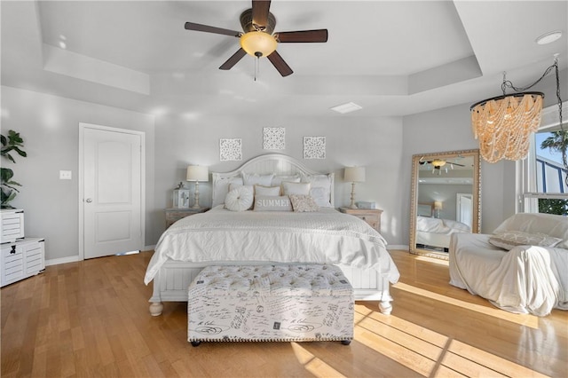 bedroom featuring a raised ceiling, wood finished floors, baseboards, and ceiling fan