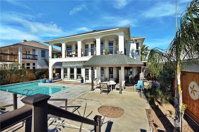 rear view of property with a balcony, a fenced in pool, fence, roof with shingles, and a patio area