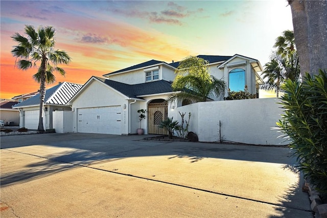 traditional-style house with driveway, a garage, a fenced front yard, and stucco siding