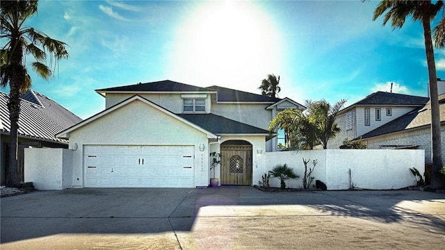 traditional-style house featuring an attached garage, driveway, a fenced front yard, and stucco siding