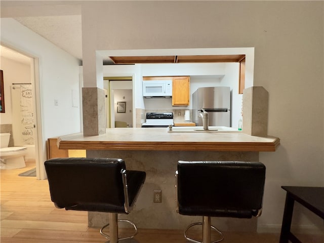 kitchen with sink, black range with electric cooktop, a kitchen breakfast bar, stainless steel fridge, and light hardwood / wood-style floors