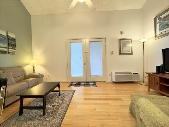 living room featuring french doors, a textured ceiling, a wall unit AC, and light hardwood / wood-style flooring