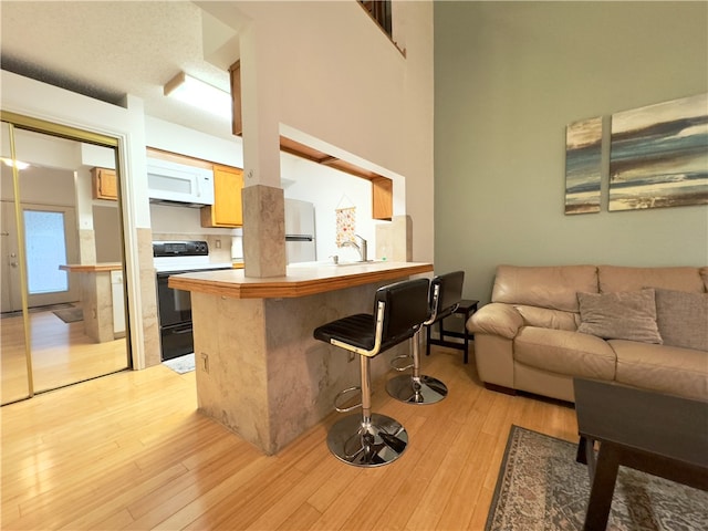 kitchen featuring kitchen peninsula, a towering ceiling, white appliances, a breakfast bar area, and light wood-type flooring