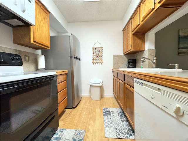 kitchen with white appliances, sink, a textured ceiling, tasteful backsplash, and light hardwood / wood-style floors