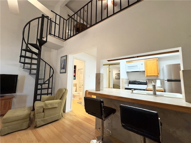 kitchen with white appliances, a towering ceiling, and light hardwood / wood-style flooring