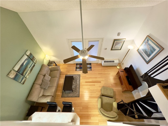 living room with a wall mounted air conditioner, a textured ceiling, ceiling fan, wood-type flooring, and high vaulted ceiling