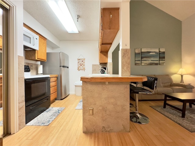 kitchen featuring a breakfast bar, black electric range oven, light hardwood / wood-style flooring, kitchen peninsula, and stainless steel refrigerator