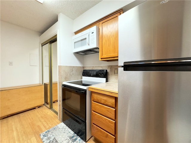 kitchen featuring stainless steel fridge, light wood-type flooring, a textured ceiling, black range with electric cooktop, and tasteful backsplash