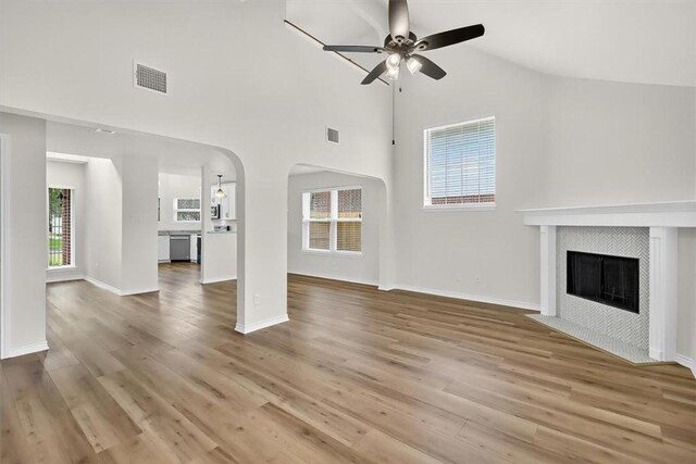 7821 Kingshire Dr, Corpus Christi, TX 78413 - unfurnished living room featuring a ceiling fan, a tile fireplace, arched walkways, wood finished floors, and high vaulted ceiling
