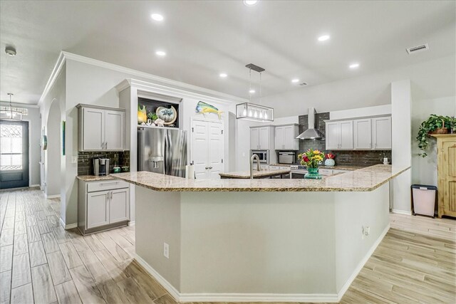 kitchen featuring stainless steel appliances, wall chimney range hood, pendant lighting, and crown molding