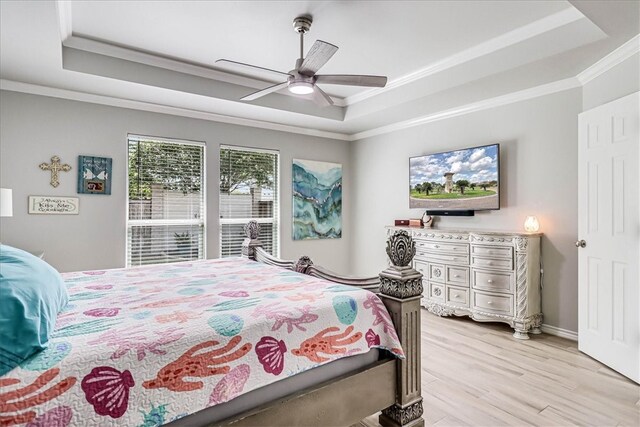 bedroom featuring light wood-type flooring, ceiling fan, crown molding, and a tray ceiling