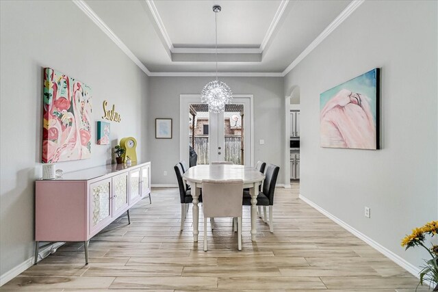 dining room featuring a tray ceiling, a notable chandelier, ornamental molding, and light hardwood / wood-style flooring