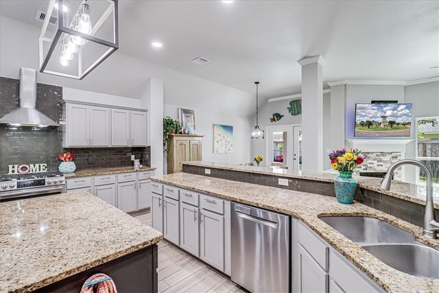 kitchen featuring light stone counters, sink, wall chimney range hood, backsplash, and appliances with stainless steel finishes