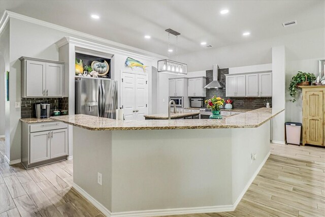 kitchen featuring pendant lighting, wall chimney range hood, appliances with stainless steel finishes, and light wood-type flooring