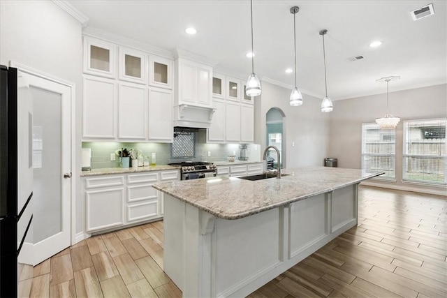 kitchen with decorative light fixtures, a kitchen island with sink, stainless steel gas stove, white cabinets, and sink