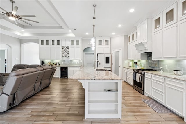 kitchen with white cabinetry, an island with sink, stainless steel gas range oven, a tray ceiling, and pendant lighting