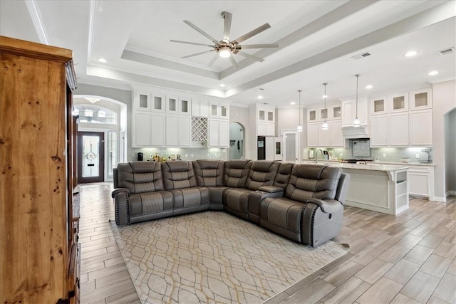 living room featuring ceiling fan, crown molding, a tray ceiling, and sink