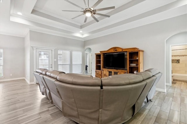 living room featuring a raised ceiling, ceiling fan, and ornamental molding