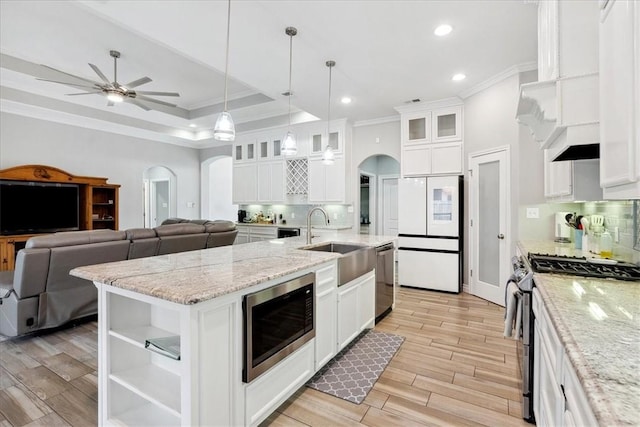 kitchen featuring a tray ceiling, white cabinets, stainless steel appliances, and a kitchen island with sink