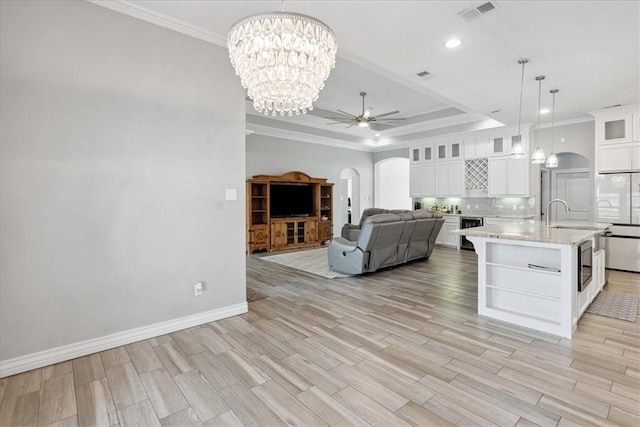 kitchen featuring ceiling fan with notable chandelier, pendant lighting, white cabinets, an island with sink, and a tray ceiling