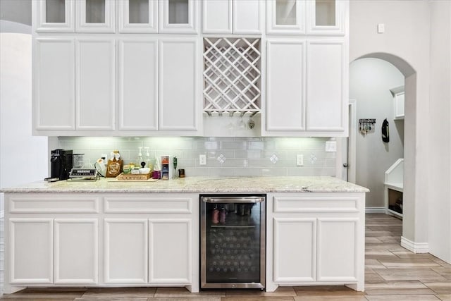 bar featuring white cabinetry, decorative backsplash, wine cooler, and light stone countertops