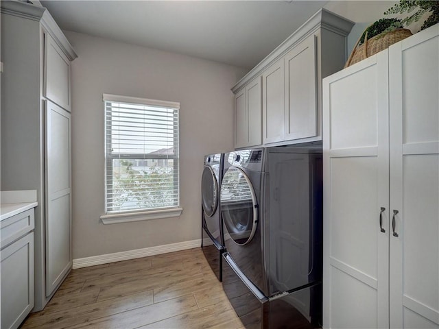 laundry area with light wood finished floors, washer and clothes dryer, cabinet space, and baseboards