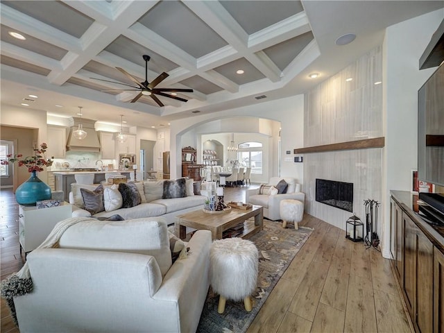 living area featuring light wood-style floors, plenty of natural light, arched walkways, and coffered ceiling