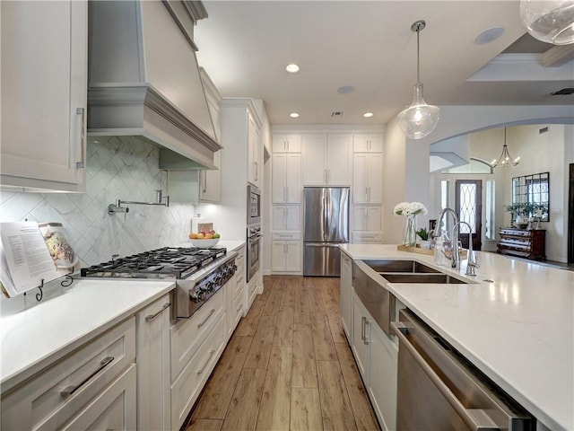 kitchen with custom exhaust hood, white cabinetry, appliances with stainless steel finishes, and decorative light fixtures