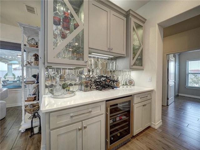 bar featuring wine cooler, visible vents, a dry bar, decorative backsplash, and light wood finished floors