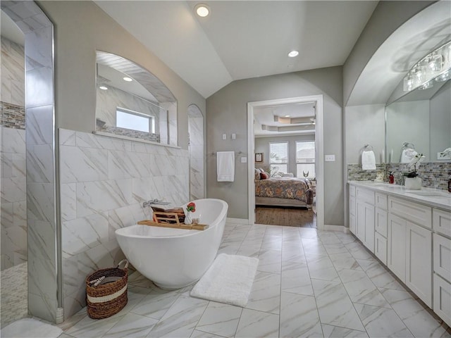 ensuite bathroom featuring marble finish floor, lofted ceiling, connected bathroom, vanity, and a freestanding tub