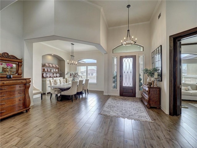 foyer entrance with a chandelier, a high ceiling, wood finished floors, baseboards, and ornamental molding