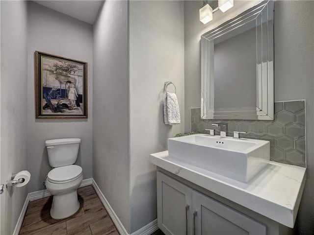 half bath with baseboards, decorative backsplash, toilet, wood finished floors, and vanity