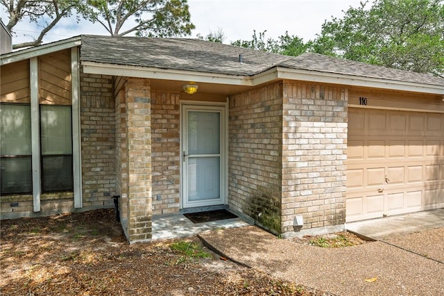 entrance to property featuring an attached garage, roof with shingles, and brick siding