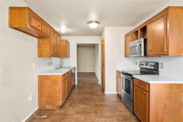 kitchen featuring brown cabinets, light countertops, a sink, baseboards, and appliances with stainless steel finishes