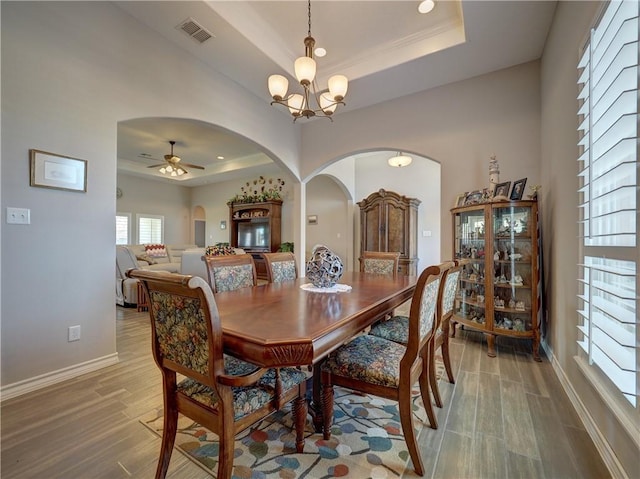 dining room featuring ceiling fan with notable chandelier, hardwood / wood-style floors, and a tray ceiling