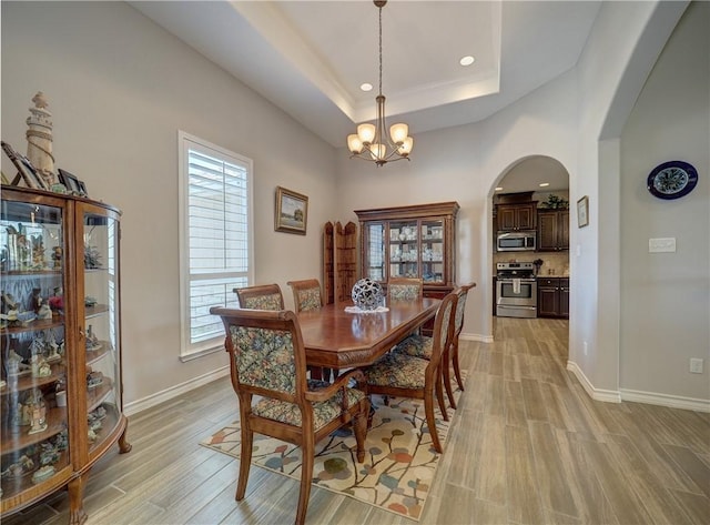 dining room featuring a notable chandelier, light hardwood / wood-style flooring, a raised ceiling, and plenty of natural light