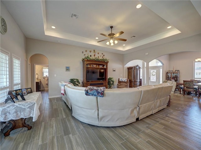 living room featuring ceiling fan, a raised ceiling, and wood-type flooring