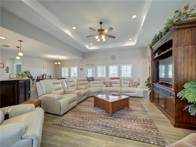 living room with ceiling fan with notable chandelier, sink, and a tray ceiling