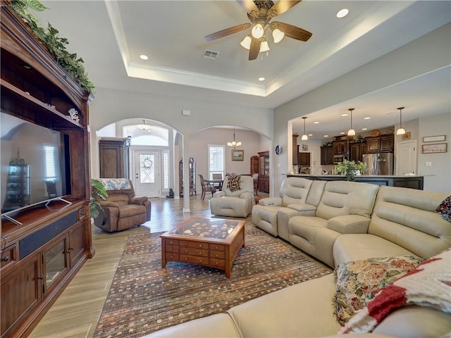 living room with a raised ceiling and ceiling fan with notable chandelier