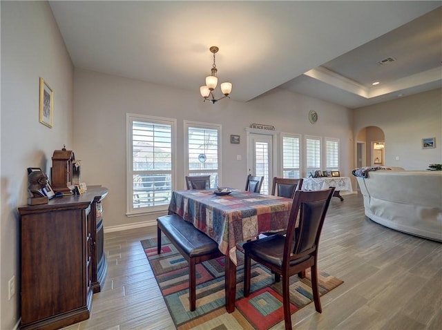 dining space with a raised ceiling, a chandelier, a healthy amount of sunlight, and light hardwood / wood-style flooring