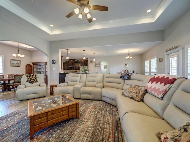 living room with ceiling fan with notable chandelier, hardwood / wood-style flooring, a tray ceiling, and crown molding