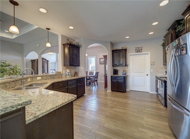 kitchen with sink, stainless steel appliances, dark brown cabinetry, and hanging light fixtures